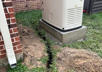 A generator sits on a concrete pad beside a brick building. A trench runs through the grass from the building to the generator.