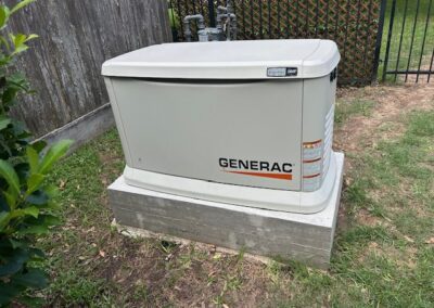 A Generac generator sits on a concrete platform next to a wooden fence and grass.