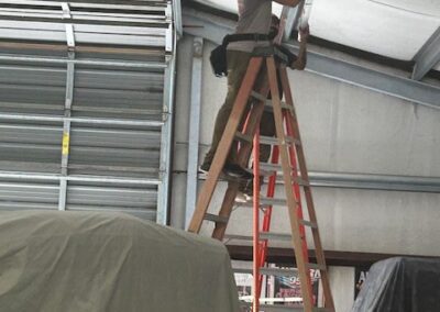 Person standing on a ladder inside a large metal structure, adjusting something on the ceiling.