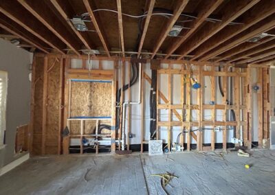 Interior view of a house under renovation, showing exposed wooden framing and electrical wiring on walls and ceiling.