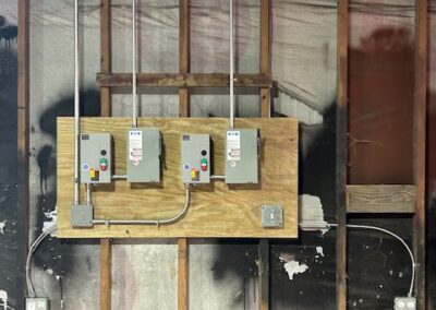 Three electrical boxes mounted on a wooden board against an unfinished wall, with exposed wiring and conduit pipes.